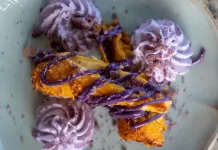 Ube Haupia Cheesecake Eggrolls By Chef Mari Wills Crispy ube haupia cheesecake eggrolls drizzled with purple ube sauce and served with whipped cream on a plate.
