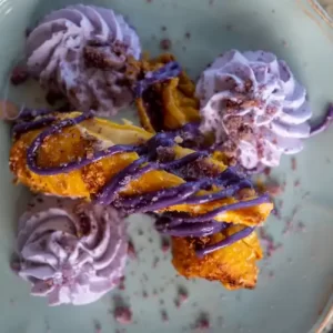 Top-down view of Hawaiian-style ube haupia cheesecake eggrolls garnished with ube cookie crumble and coconut drizzle.