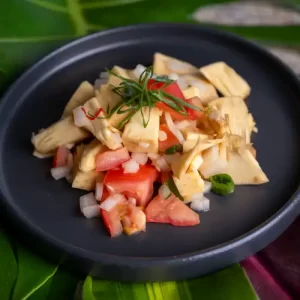 Overhead view of prepared ʻulu (breadfruit) poke recipe ingredients cubed ʻulu, red tomatoes, and Maui onions—gently tossed with a shoyu-sesame oil dressing and fresh green onions in a matte black bowl.